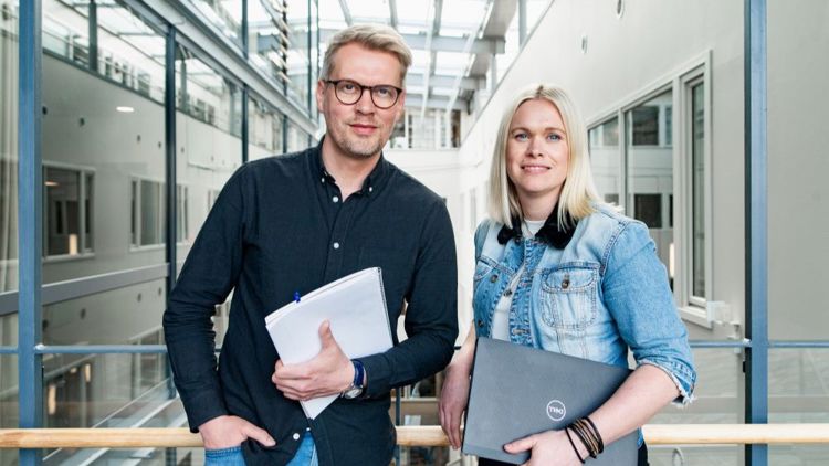 Bildet viser to kolleger som står ved siden av hverandre. De har blokk og PC i hendene og ser rett i kameraet.